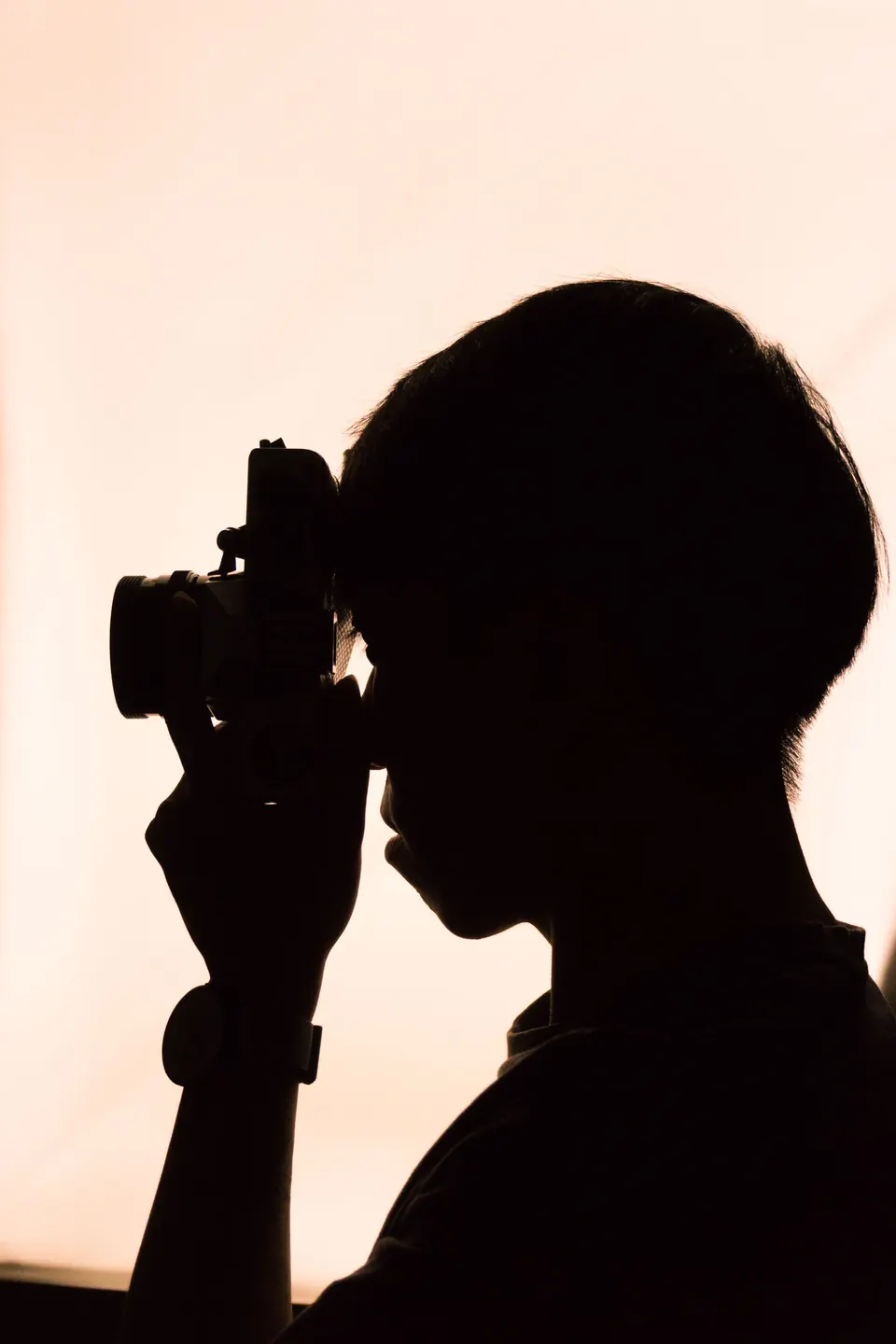 Silhouette of a photographer raising a camera against a soft peach sky