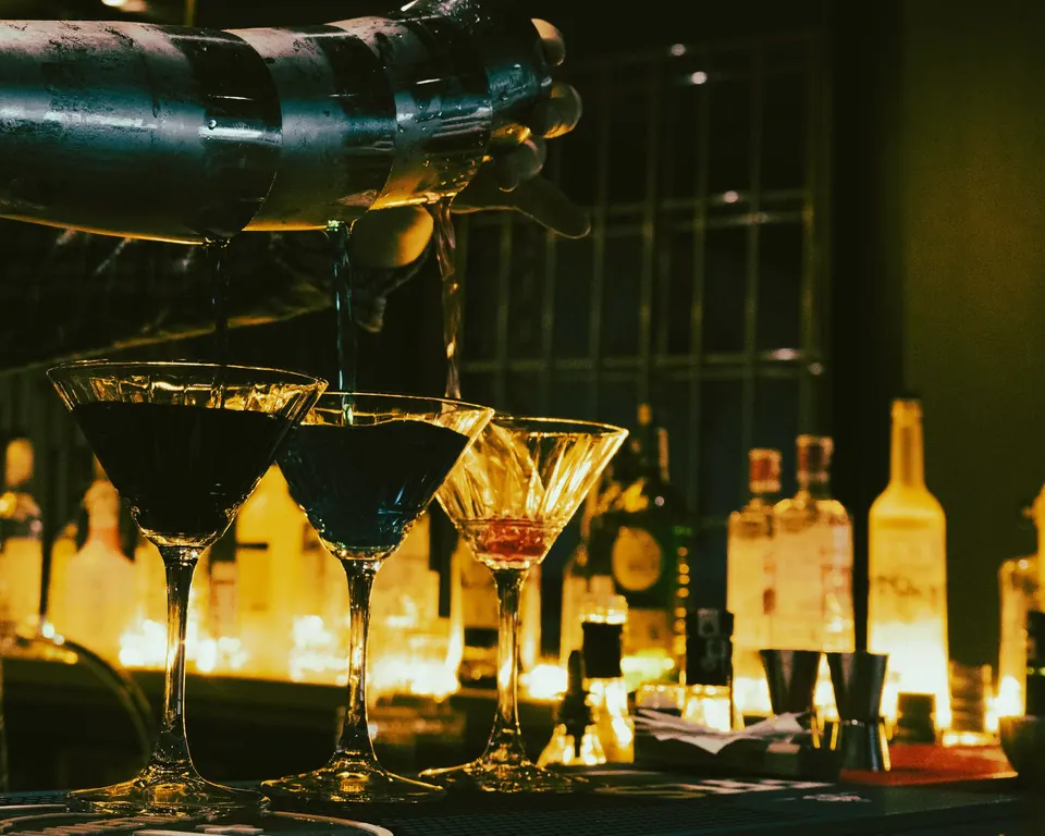 Martini glasses lined up along a glowing back bar