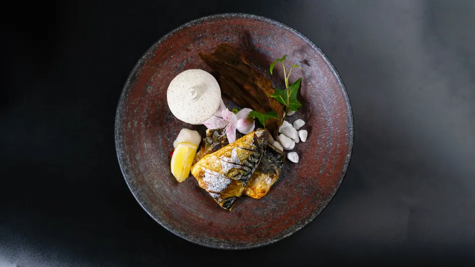 Overhead view of a fine-dining fish course on a dark stoneware plate