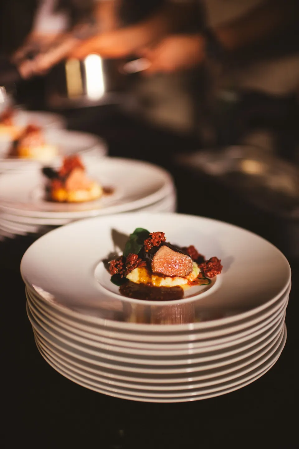 A finished plate waiting at the pass beside a stack of clean white plates
