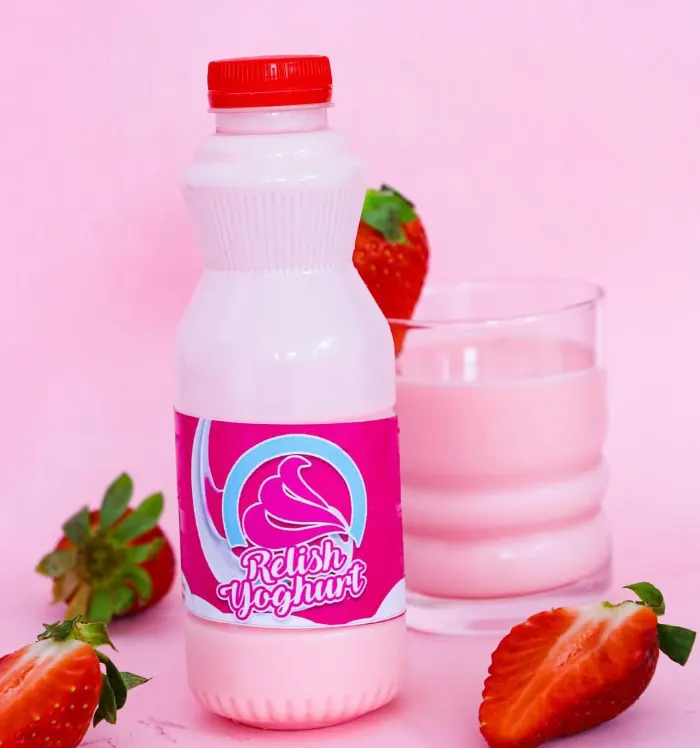 Bottle of Relish strawberry yoghurt beside a glass of yoghurt and halved strawberries on a pink backdrop