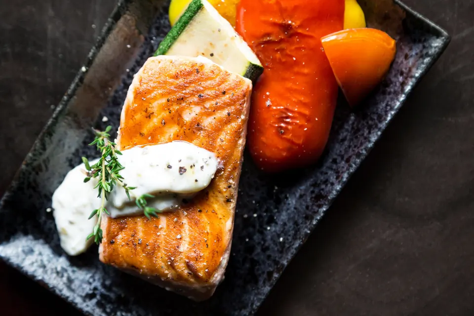 Grilled salmon fillet with herb crème and roasted peppers on a dark slate tray