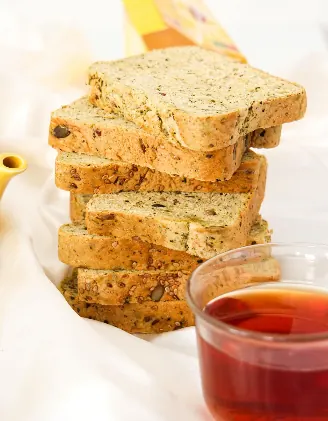 Stack of seeded wholegrain bread slices on white linen beside a glass cup of tea