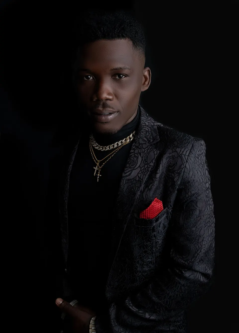 Man in a black jacket with a red pocket square against a black background