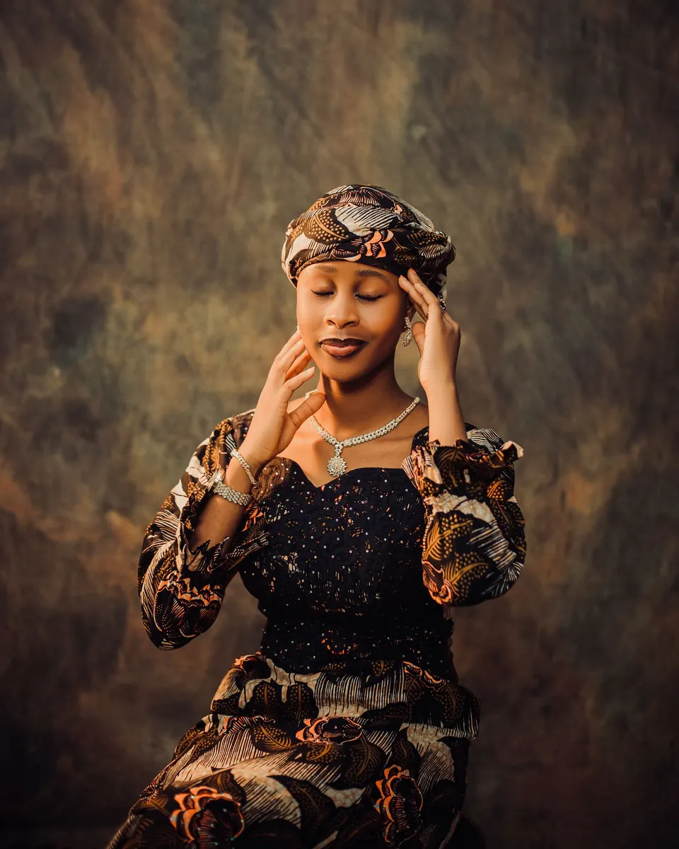 Woman in a patterned headwrap and dress against a painted backdrop