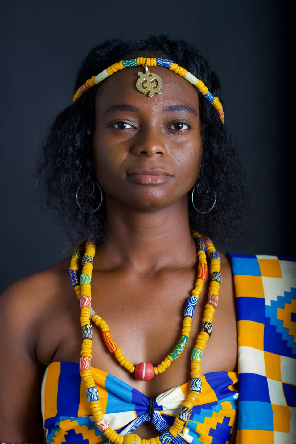 Woman wearing kente cloth and beaded jewellery in studio light