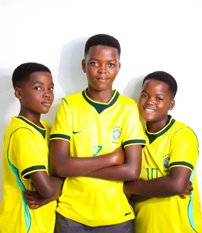 Three boys in yellow Brazil football shirts posing arm in arm against a white studio wall