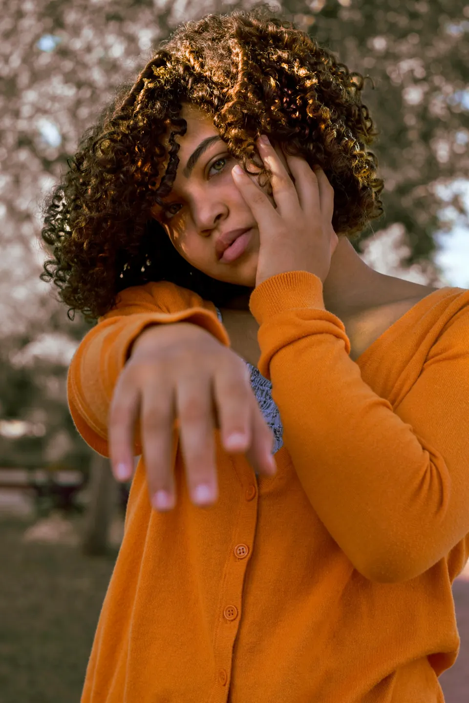 Woman with curly hair in an orange cardigan reaching toward the camera