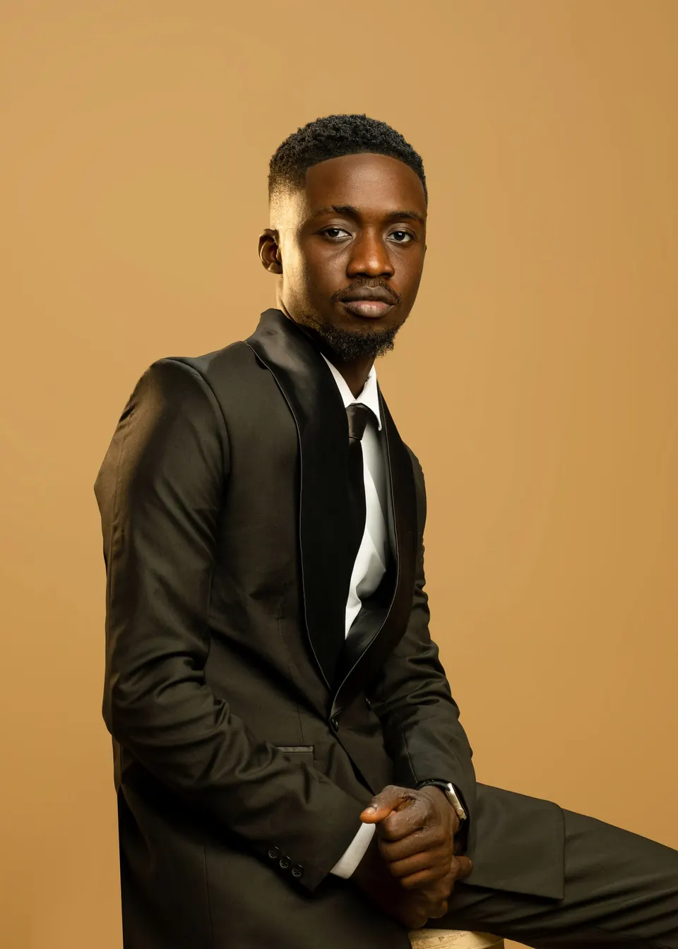 Seated man in a black suit against a warm tan studio backdrop