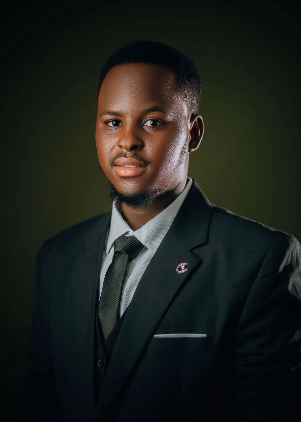 Man in a dark three-piece suit against a deep green backdrop