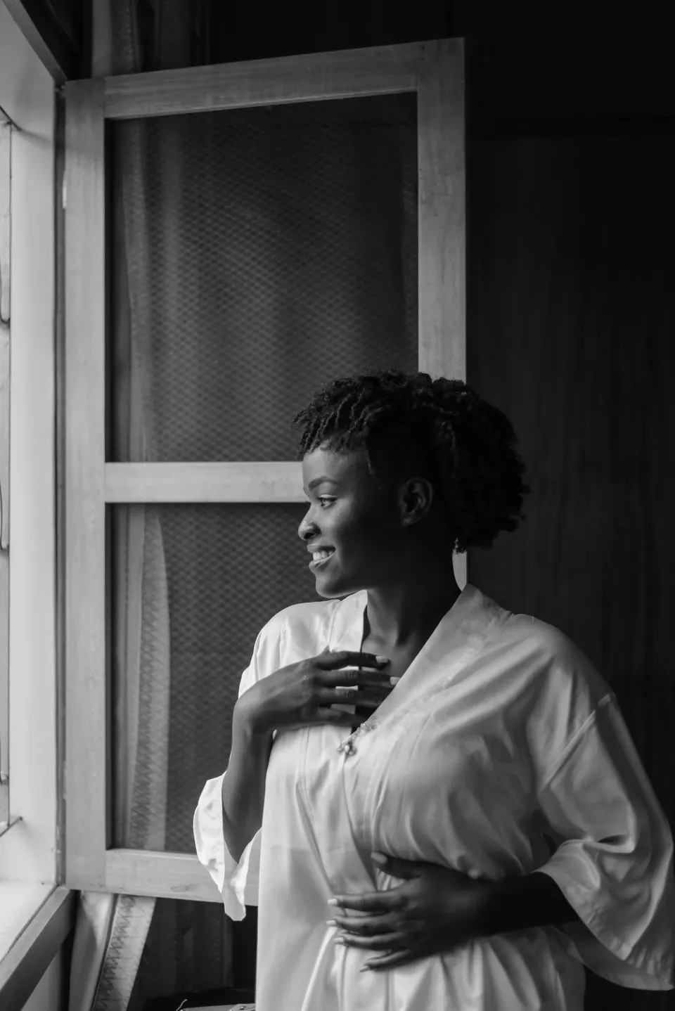 Black-and-white portrait of a woman smiling out of an open window